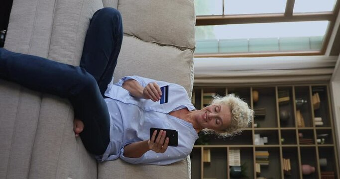 Happy cheerful mature shopper woman using credit card for online buying, making payment, typing on mobile phone, shopping on Internet stores, inserting data on ecommerce website, smiling