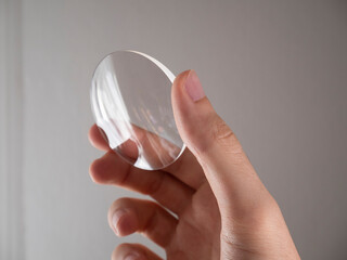 Hand holds a glass eyeglass prescription lens in the laboratory