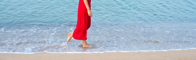 Young woman wearing red dress walking down the sand beach on sea summer vacation