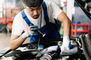 Asian Mechanic working and checking engine in garage, Professional technician is wearing gloves and shine a flashlight on the car, Car Service and Automobile Maintenance Concept