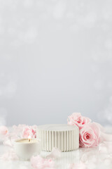 Marble podium with pink roses, petals and candles on a white table with the bokeh effect. Concept scene stage showcase for new product, promotion sale, banner, presentation, cosmetic. Soft image style