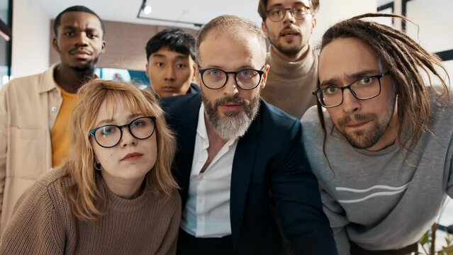 A multinational team of 3d game developers in the office looks at the camera as if it were a monitor and actively discusses the project.