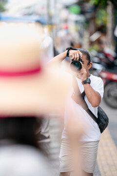 Professional Asian Camera man focus on the image with his mirrorless camera beside the street outdoor field.