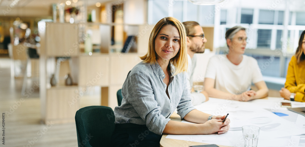 Wall mural Confident young designer sitting in a meeting with her team