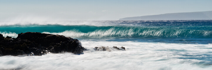 A large, long blue wave crashes on the shores of Maui Hawaii near La Perouse Bay.