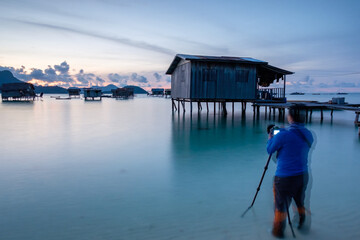 Semporna, Sabah, Malaysia - 27/7/2022 : Alone nature Muslim Photographer shoots the seascape with Bajau Lau Villages at Maiga Island, Semporna, Sabah. - obrazy, fototapety, plakaty