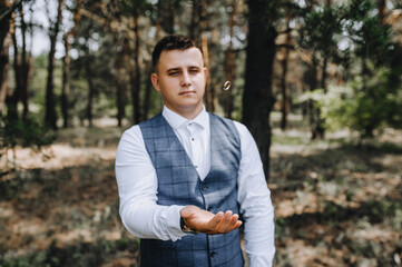 A stylish, young groom tosses a golden ring while standing in a forest in nature. Wedding portrait, photography.