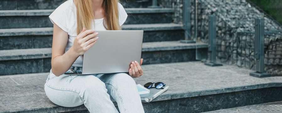 female student sitting with laptop on stairs near university smiling and studying