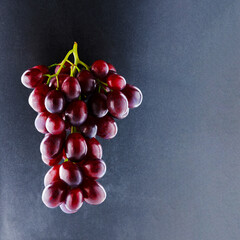 Shiny bunch of ripe backlit grapes on textured black background