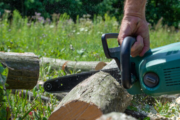 A male uses a chainsaw to cut up a log into firewood.