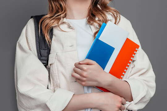 female student holding backpack, book, notebook, passport isolated on a dark grey background, copy space, immigration, paperwork
