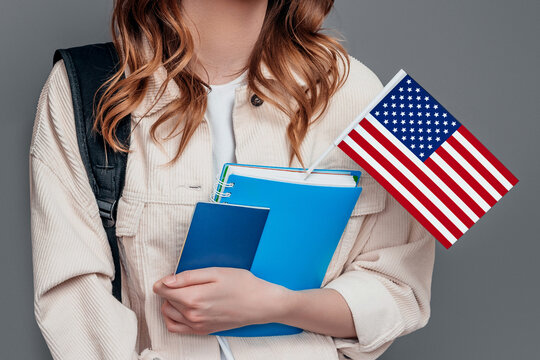 female student holding backpack, book, notebook, passport and USA flag isolated on a dark grey background, copy space