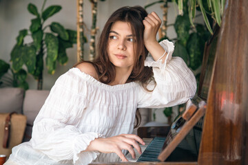 A beautiful young woman plays the old wooden piano.