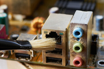 Brush cleaning an old computer board from dust and dirt. Close-up.