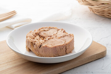 Canned tuna steak in brine on white plate on wooden table