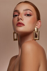 Model with red hair, brown eyes and freckles, poses, beauty shoot. She wears gold rectangle...