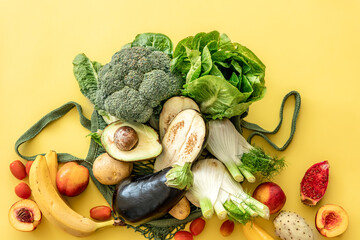 Fresh green vegetables and fruits in a green string bag on a yellow background.