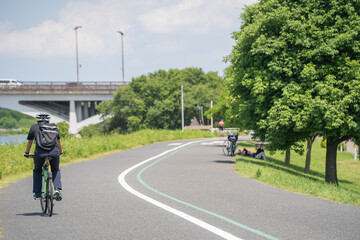Obraz premium 手賀沼のサイクリングロード、自転車と木陰で昼寝する人（6月初旬の晴れの日）