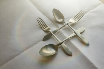 Intertwined spoons and forks with an iridescent light effect viewed from above on a wrinkled white background