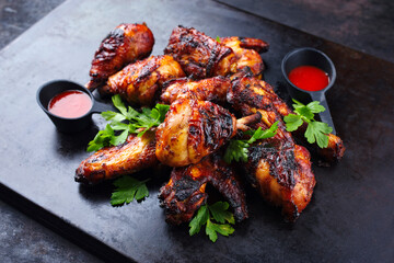 Traditional barbecue chicken wings and drumsticks with hot chili mango sauce and coriander served...