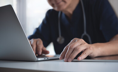 Close up of doctor working on laptop computer and using digital tablet on table in doctor's office, medical research, healthcare and medicine concept