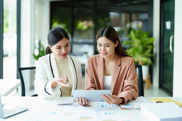 Two Asian businesswoman using a tablet and documents to work.