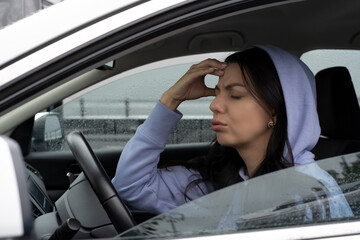 A young woman sits in her car and has headache. Tired woman on road traffic.