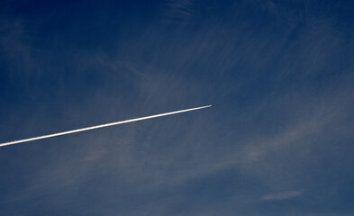 A plane flying in the blue sky and clouds. A white contrail from an airplane in the summer sky.