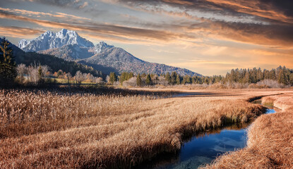 Majestic mountains in the distance with lush scenic fields of meadows and a river during sunset. Amazing nature scenery with colorful sky. Wonderful nature bakground. retro effect . Creative image
