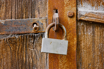Old rusty padlock on wooden gates. An obsolete lock hangs on the weathered door.