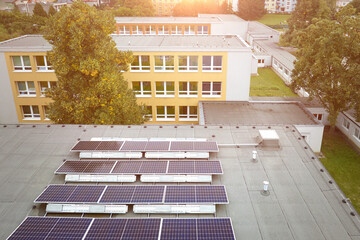 Solar power plant on the school roof. View of the photovoltaic panels against the school buildings, orange and blue colors. Fighting the energy crisis.