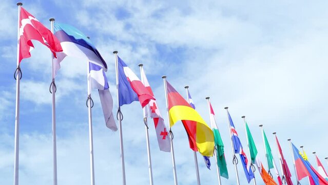 national flags of Europe and other countries on satin flutter in wind in blue sky near building of European Parliament, state symbols, concept of international cooperation, global business