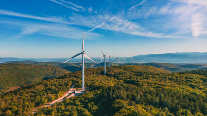 View of a wind farm in a mountainous forest field with mountains in the background. View during the...