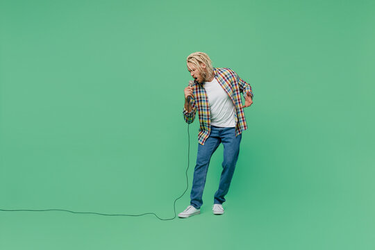 Full body singer young blond man with dreadlocks 20s wear casual shirt sing song in microphone at karoke club isolated on pastel plain light green background studio portrait. People lifestyle concept.