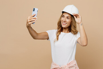 Fototapeta na wymiar Young employee laborer handyman woman in white t-shirt helmet do selfie shot on mobile cell phone isolated on plain beige background Instruments accessories for renovation room. Repair home concept.