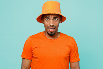 Young irritated disappointed sad shocked man of African American ethnicity 20s wearing orange t-shirt hat looking camera isolated on plain pastel light blue cyan background. People lifestyle concept.