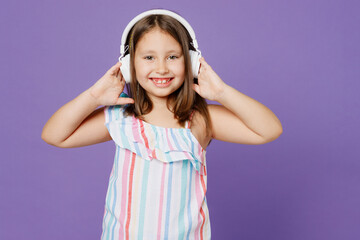 Little smiling happy cheerful kid child girl 5-6 years old wearing striped dress headphones listen music isolated on plain pastel light purple background. Mother's Day love family lifestyle concept.