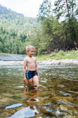 A child stands in a mountain river against the background of a forest, children's vacations in nature, swimming in cold water, clear waters of the river.