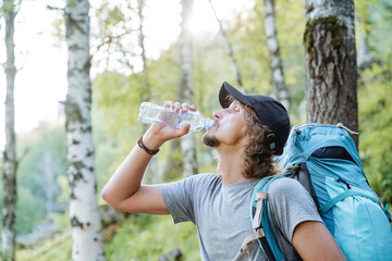 A guy drinks water in the woods with a backpack standing on the trail, hiking in Europe, a curly...