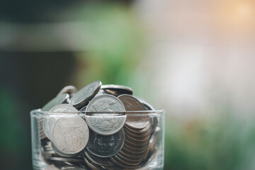 Full of coin in a glass jar concept for business, economy, financial, investment, saving, money, bank, loan, deposit and retirement. Development idea to success, green nature background.