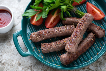 Close-up of barbecued balkan cevapcici or skinless beef sausages on a green serving pan, selective focus, horizontal shot