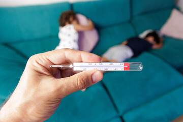 Thermometer in the hand of an adult and children with fever lying in the background