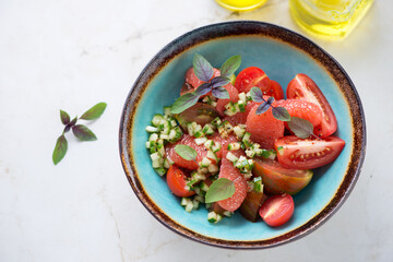 Salad with grapefruit, tomatoes and cucumber tartar served in a turquoise bowl, elevated view on a light-beige marble background, horizontal shot