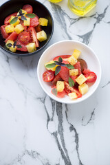 Bowls of salad with grapefruit, tomatoes and yellow watermelon on a white marble background, vertical shot with space, high angle view