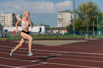 Fototapeta premium Young woman running on the running track at the stadium outdoors