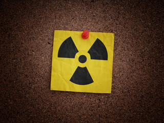 A yellow paper note with a radiation warning sign on it pinned to a corkboard