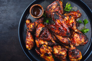 Traditional barbecue chicken wings and drumsticks with hot chili mango sauce and coriander served as top view on a rustic board with copy space left