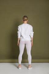 Attractive blonde woman in white sweatshirt and leggings on green background. Mock-up.