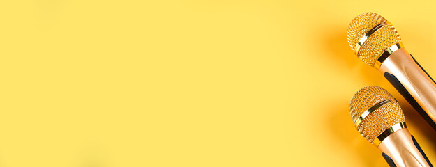 Two golden microphones isolated on yellow background close up