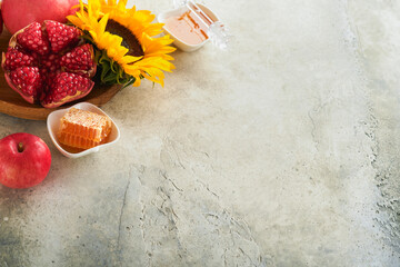 Rosh Hashanah. Ripe pomegranate, apple, honey and sunflower, yellow flowers on rustic grey background. Composition with symbols autumn jewish Rosh Hashanah holiday attributes. Top view with copy space